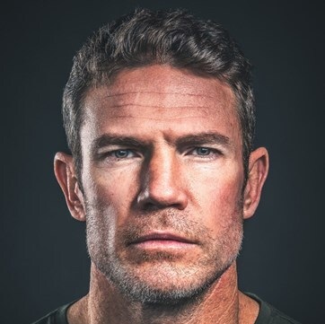 Headshot image of a white man in his early 40s with rugged features, dark hair and eyes, and a strong jaw.